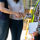Two people shaking hands with a worker in a safety vest holding a clipboard outdoors.