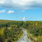 Winding highway through autumn forest under a blue sky with clouds
