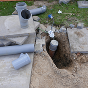 PVC pipes and fittings beside a dug trench in a concrete yard during plumbing work