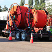 Two large orange cable reels on a trailer, with traffic cones on a road site.
