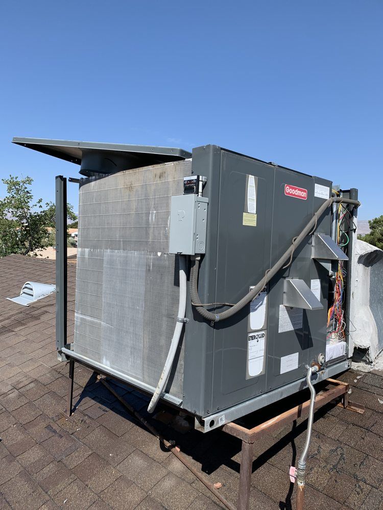 A grey HVAC unit sitting on a metal stand on a residential roof against a clear blue sky.