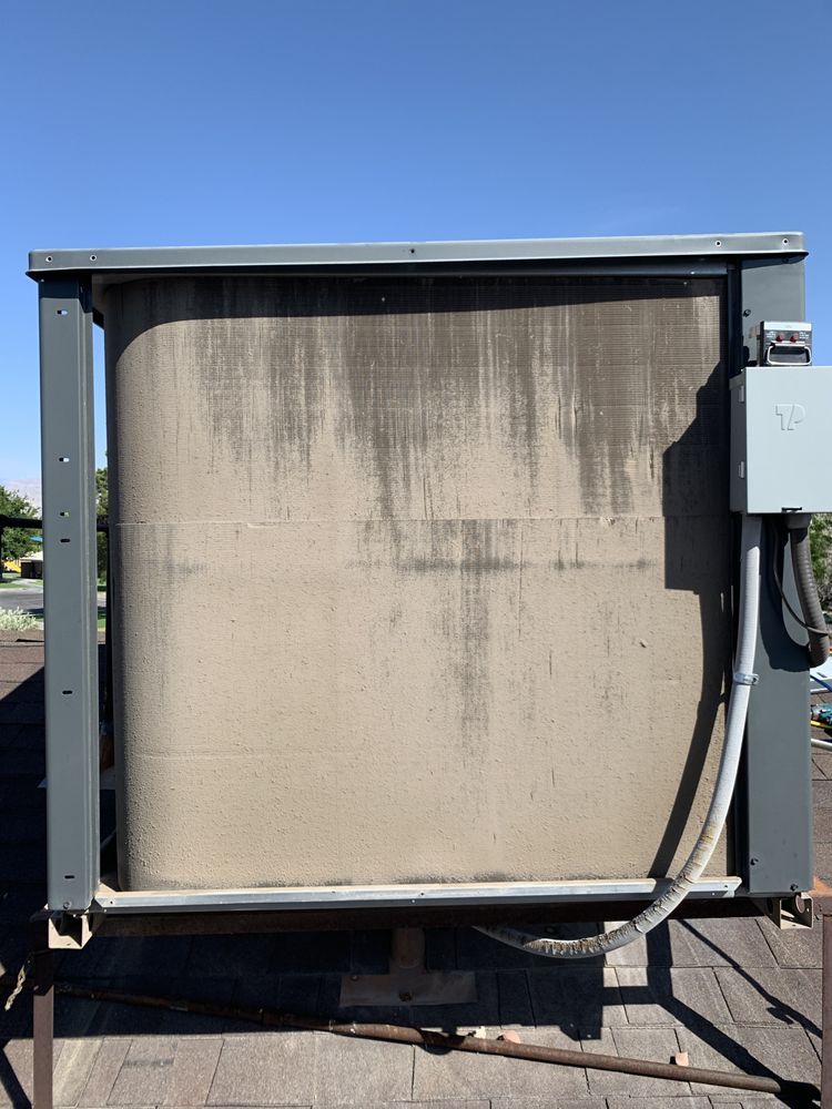 An outdoor rooftop HVAC unit condenser coil with visible dirt accumulation, viewed from the side with an electrical box.