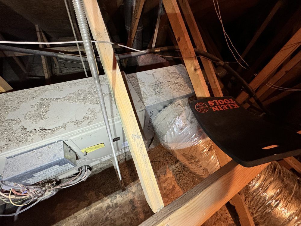 An attic HVAC air handler unit with connected flexible ductwork situated among wooden roof trusses.