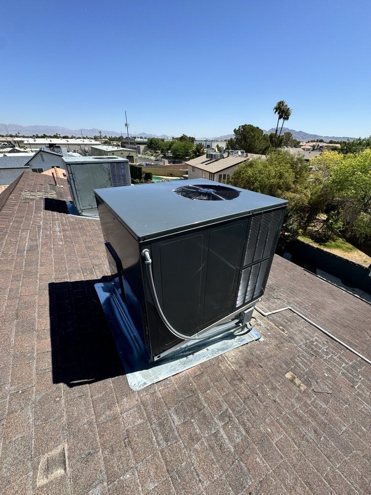 A rooftop HVAC unit on a shingled roof under a clear blue sky.