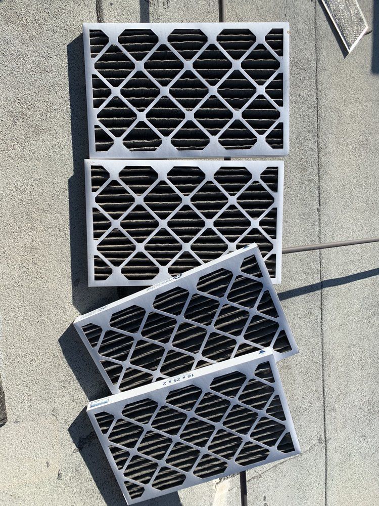 Four rectangular, dark-colored HVAC air filters arranged on a concrete surface outdoors.