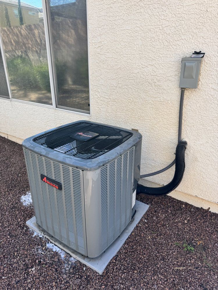 An outdoor HVAC condenser unit sits on a concrete pad next to a beige stucco wall with an electrical disconnect box.