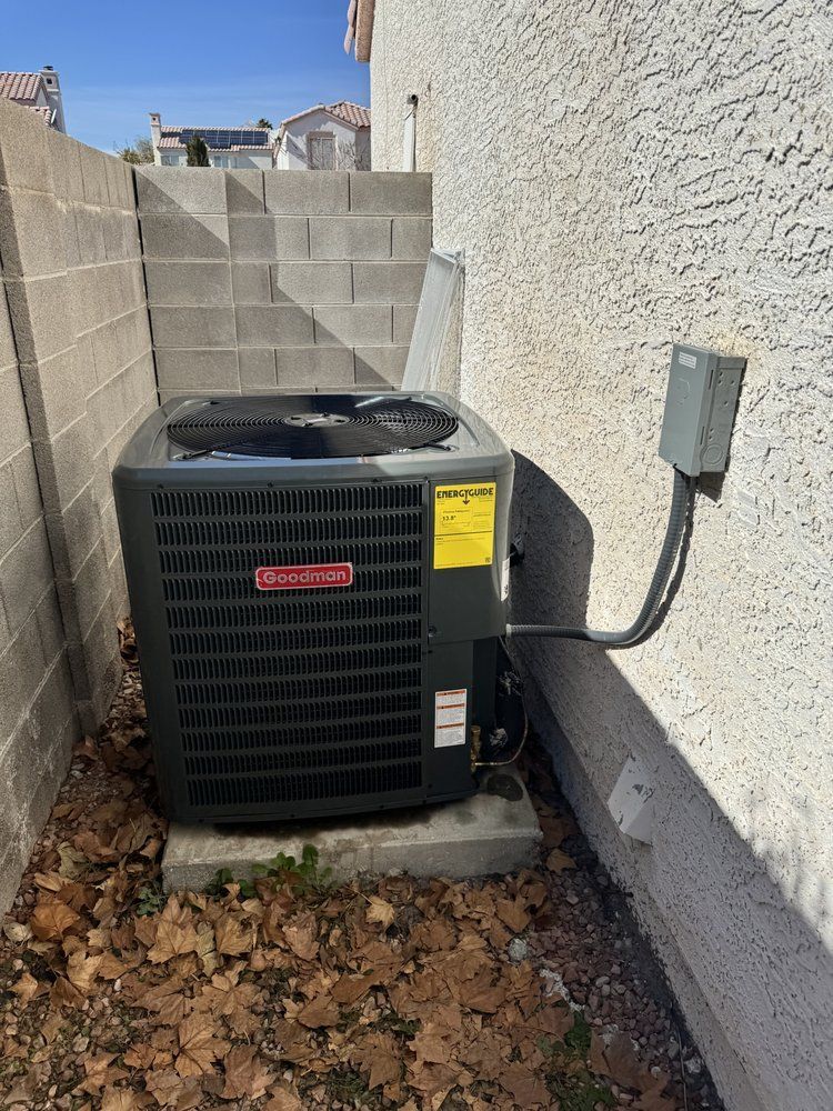 A gray outdoor air conditioning unit sits on a concrete slab next to a stucco house wall and a block fence.