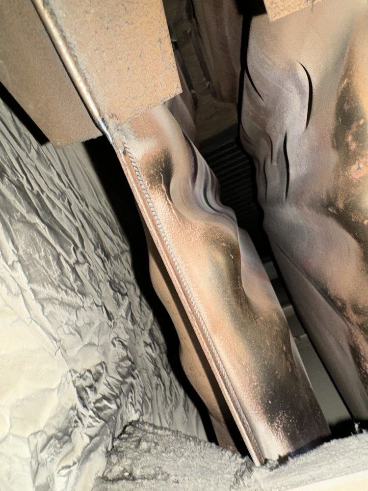 Close-up of damaged, warped metal ductwork insulation with soot staining inside an HVAC system unit.