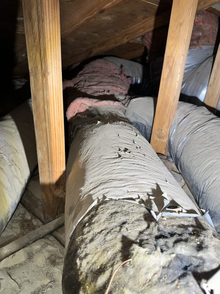 Old, damaged flexible HVAC ducts with torn insulation and visible dust in a residential attic.