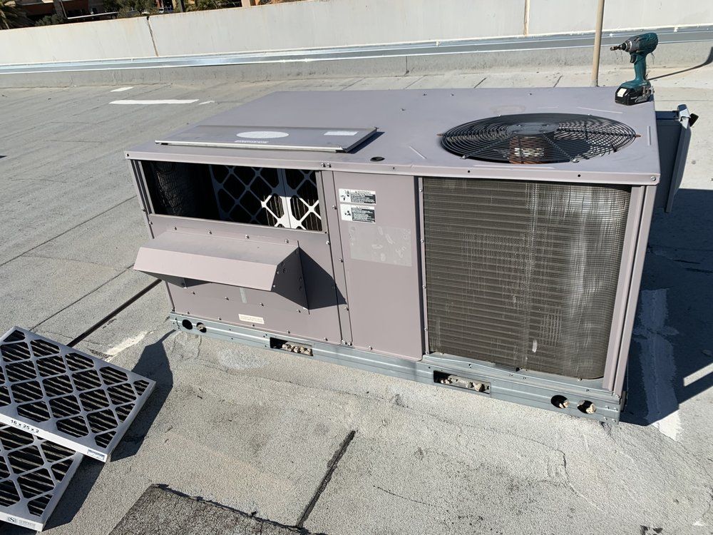 A rooftop HVAC unit with two removed air filters lying on the concrete surface nearby.