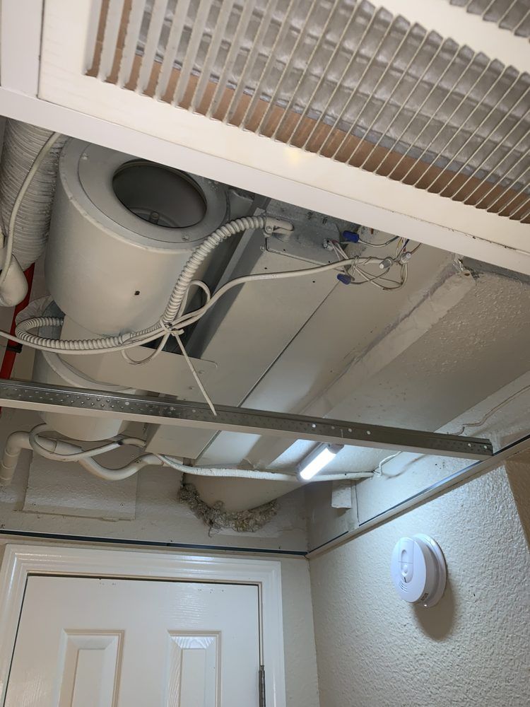 A white ceiling-mounted HVAC fan unit with visible wiring, located in an interior hallway above a door.