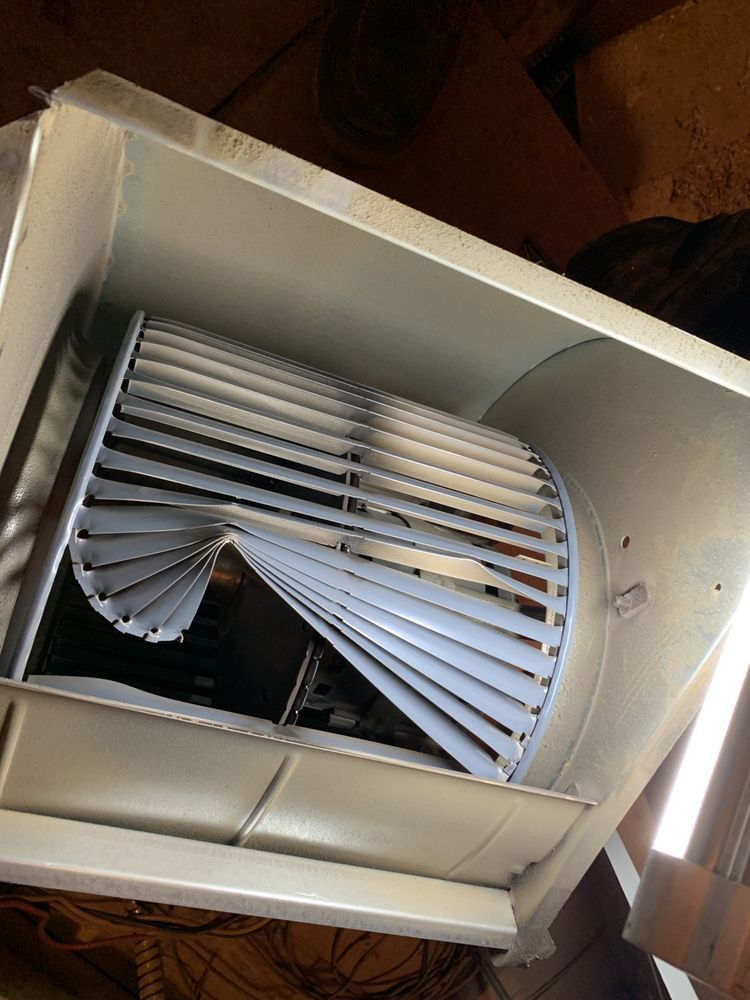 A damaged metal blower fan wheel with bent, twisted blades inside an HVAC unit housing.