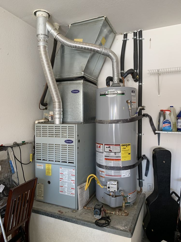 A silver gas furnace and water heater connected by a metal vent pipe, installed on a raised platform in a garage.
