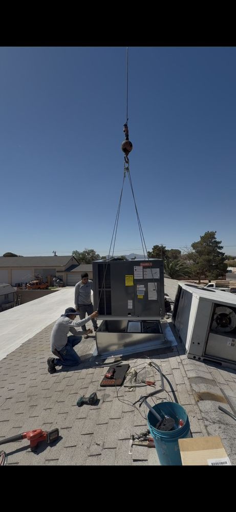 Two technicians guide a rooftop HVAC unit being lowered by a crane onto a building's roof.