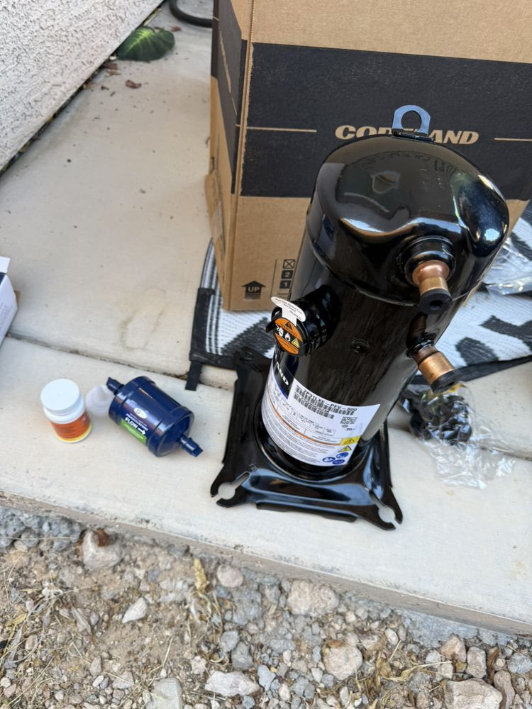 A black Copeland compressor stands on a concrete surface next to a box, a small blue filter-drier, and a pill bottle.