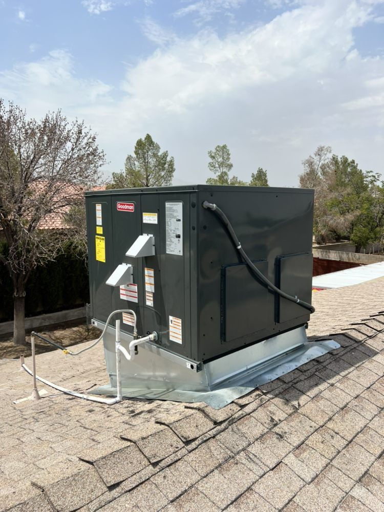 A dark gray HVAC rooftop unit installed on a shingled roof under a clear blue sky.