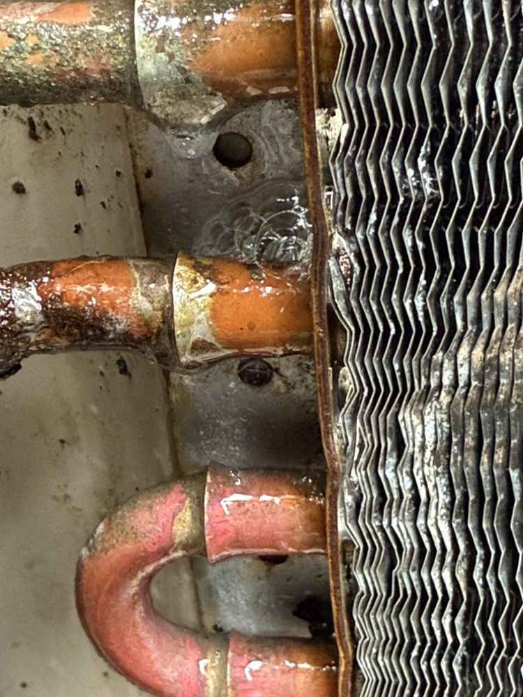 A close-up of a corroded copper pipe joint attached to an HVAC evaporator coil showing signs of a refrigerant leak.