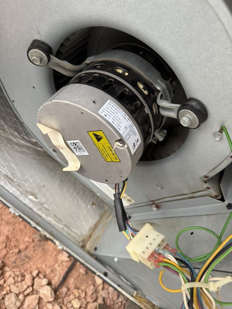 A silver blower motor inside an HVAC unit, mounted with rubber grommets and connected by a multi-pin electrical harness.