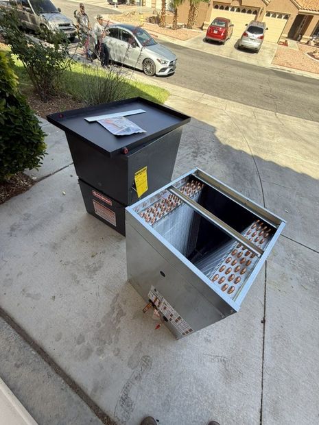 An HVAC evaporator coil unit and its metal casing sit on a residential driveway near parked cars.