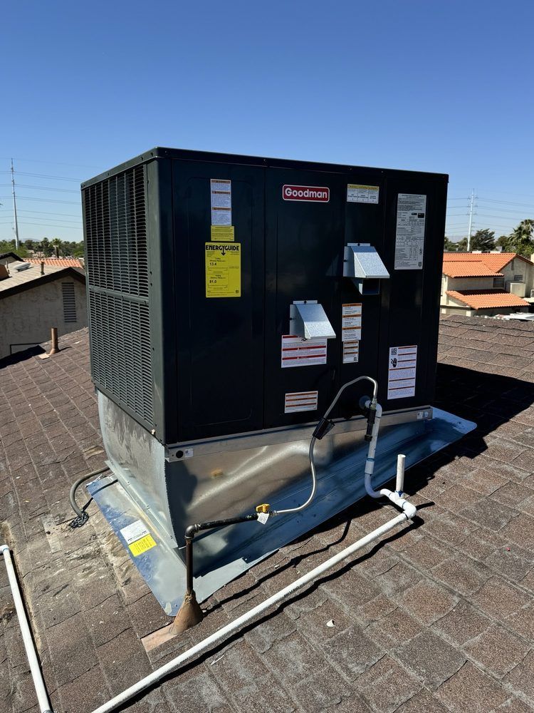 A dark-colored HVAC rooftop unit installed on a brown shingled roof under a clear blue sky.