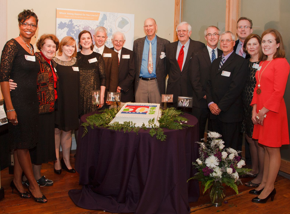 Group of people posing indoors around a decorated cake at a formal celebration