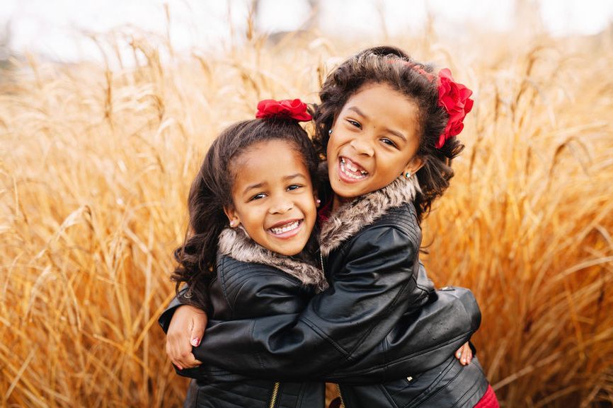 Two smiling children in black jackets hugging in a golden field