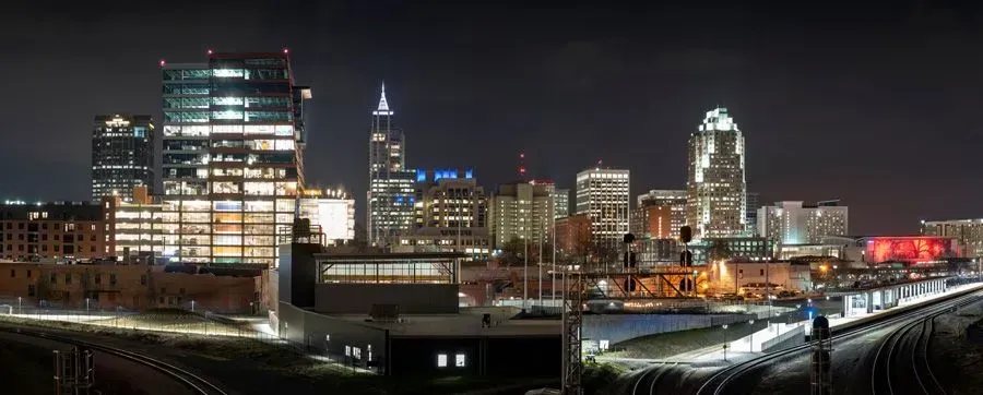 Nighttime city skyline with illuminated office buildings and rail tracks in the foreground
