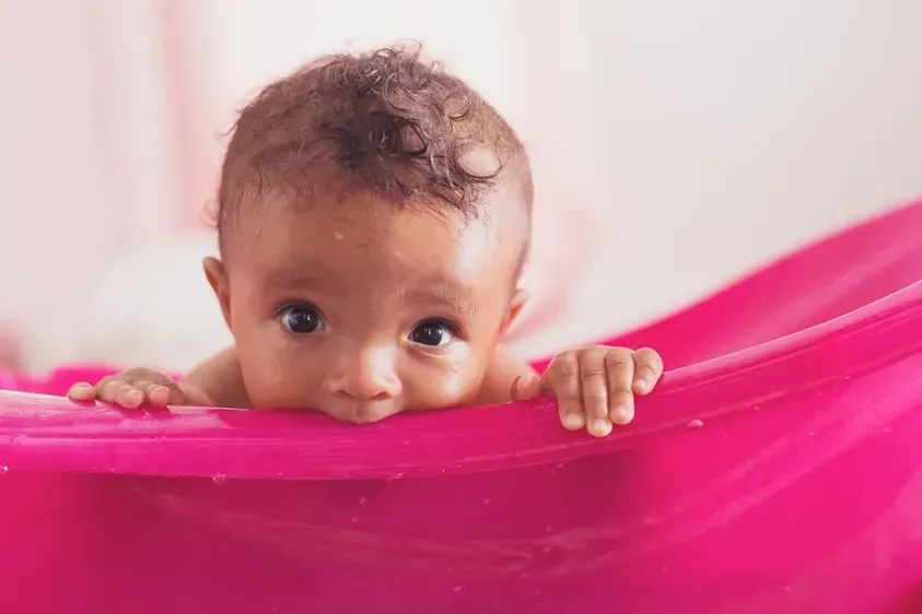Baby peeking over a bright pink fabric with hands on top and wide eyes