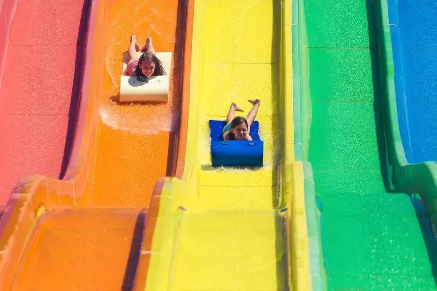 People sliding down a bright rainbow water slide, smiling in separate lanes