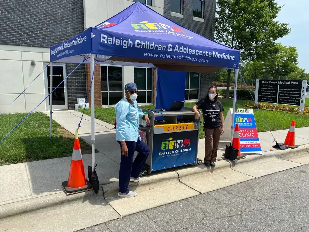 Raleigh Children’s Advocacy Center tent with two masked staff beside a table at a sidewalk outreach booth