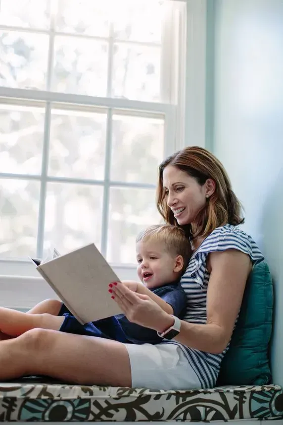 Woman reading with a child on her lap by a bright window