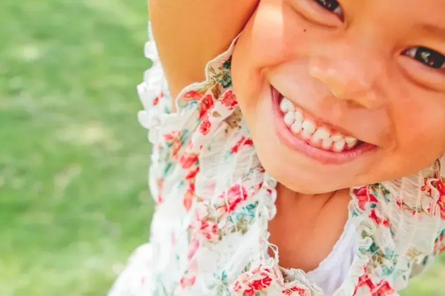 Smiling child in a floral dress on a grassy lawn, close-up with bright sunlight