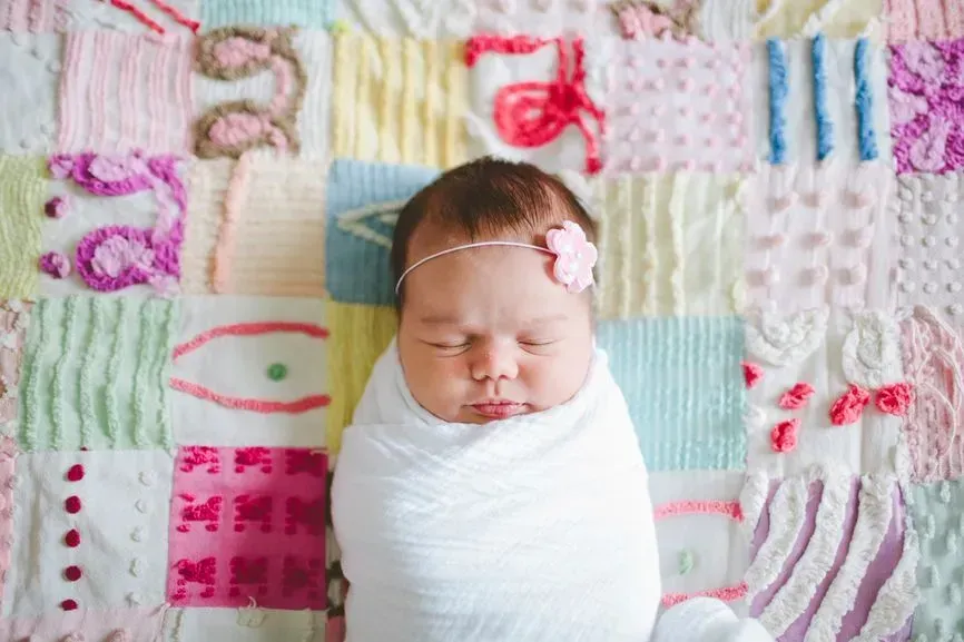 Sleeping newborn wrapped in white blanket on a pastel patchwork quilt