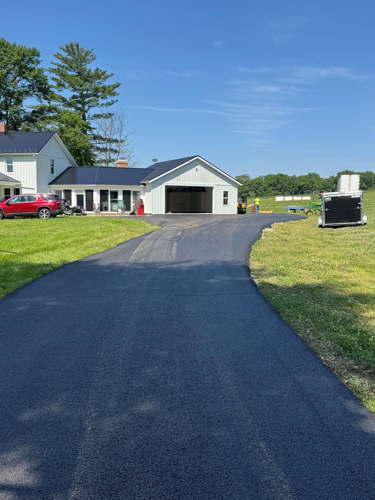 Long driveway to a white house and garage on a sunny rural property