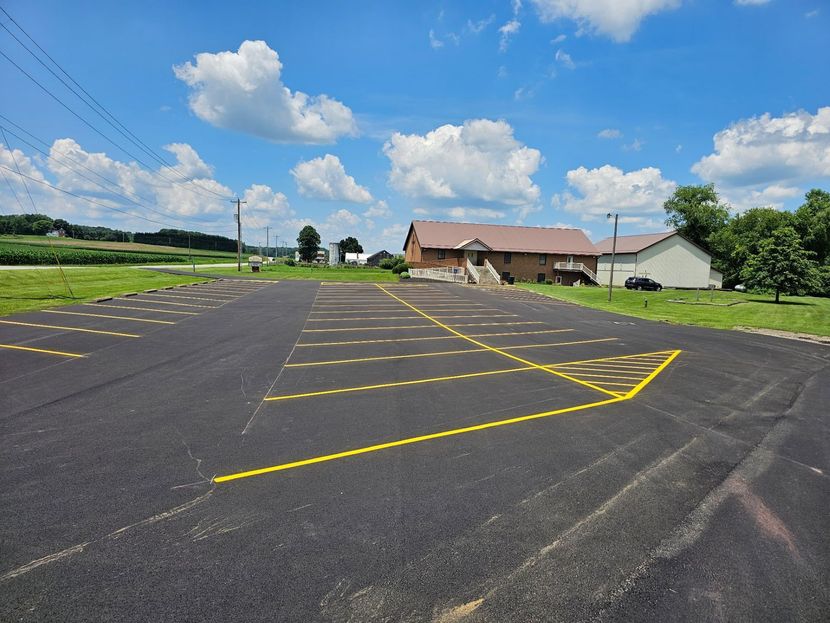 Empty parking lot with yellow lines beside a grassy field and buildings under a blue sky