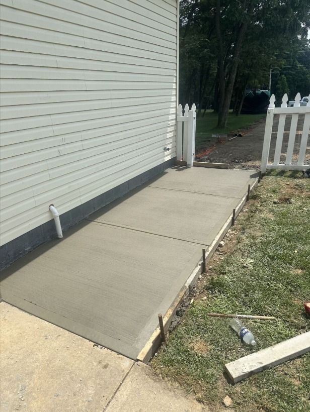 New concrete walkway beside a house, with white fence and lawn edge.