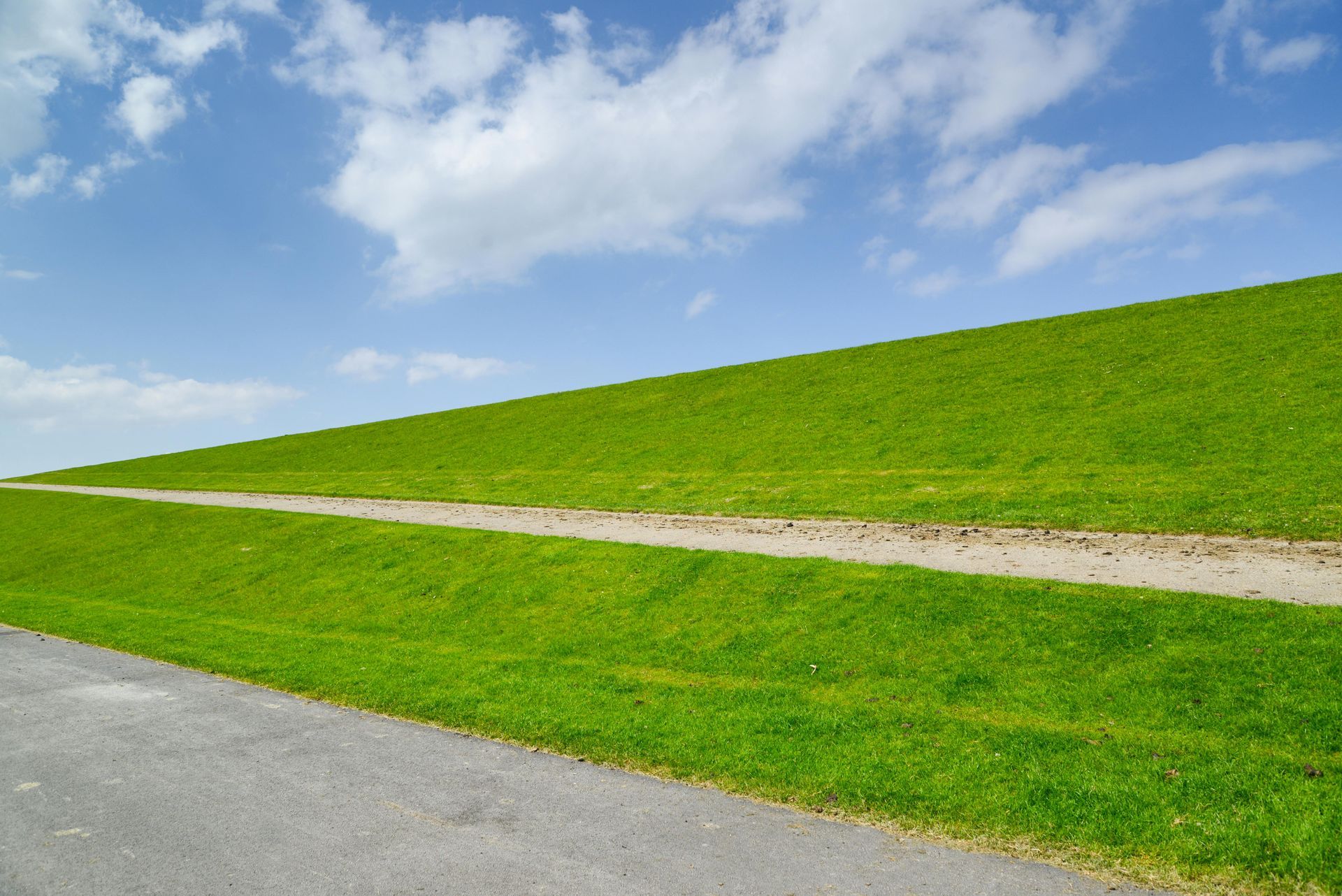 Grassy hillside with a winding gravel path under a blue sky with clouds