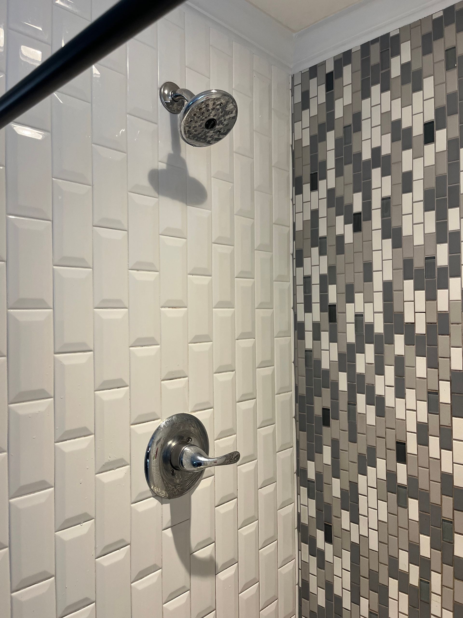 A shower with a gray and white tile wall and a shower head