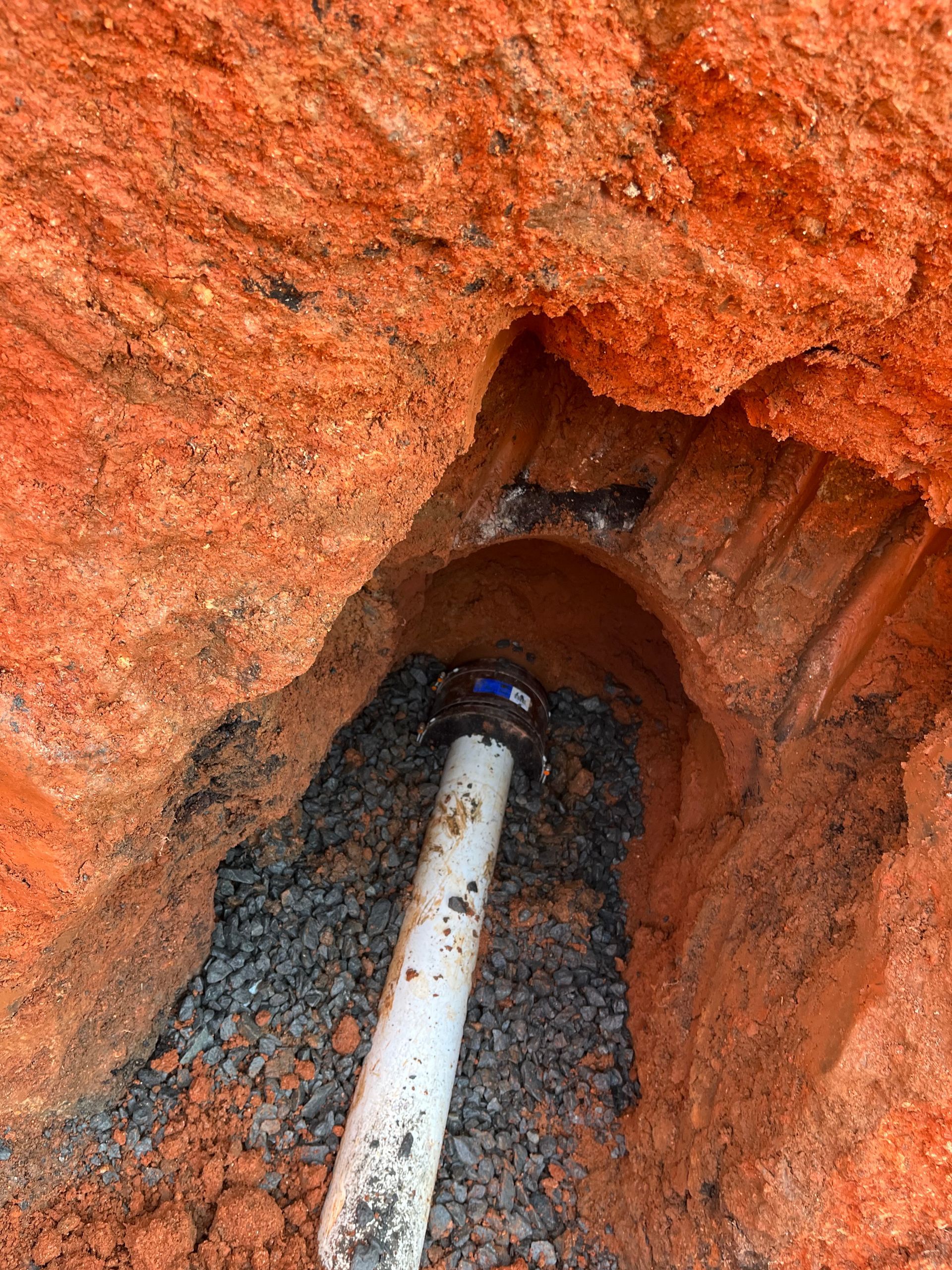 White pipe in a reddish dirt trench or hole, with gravel around it