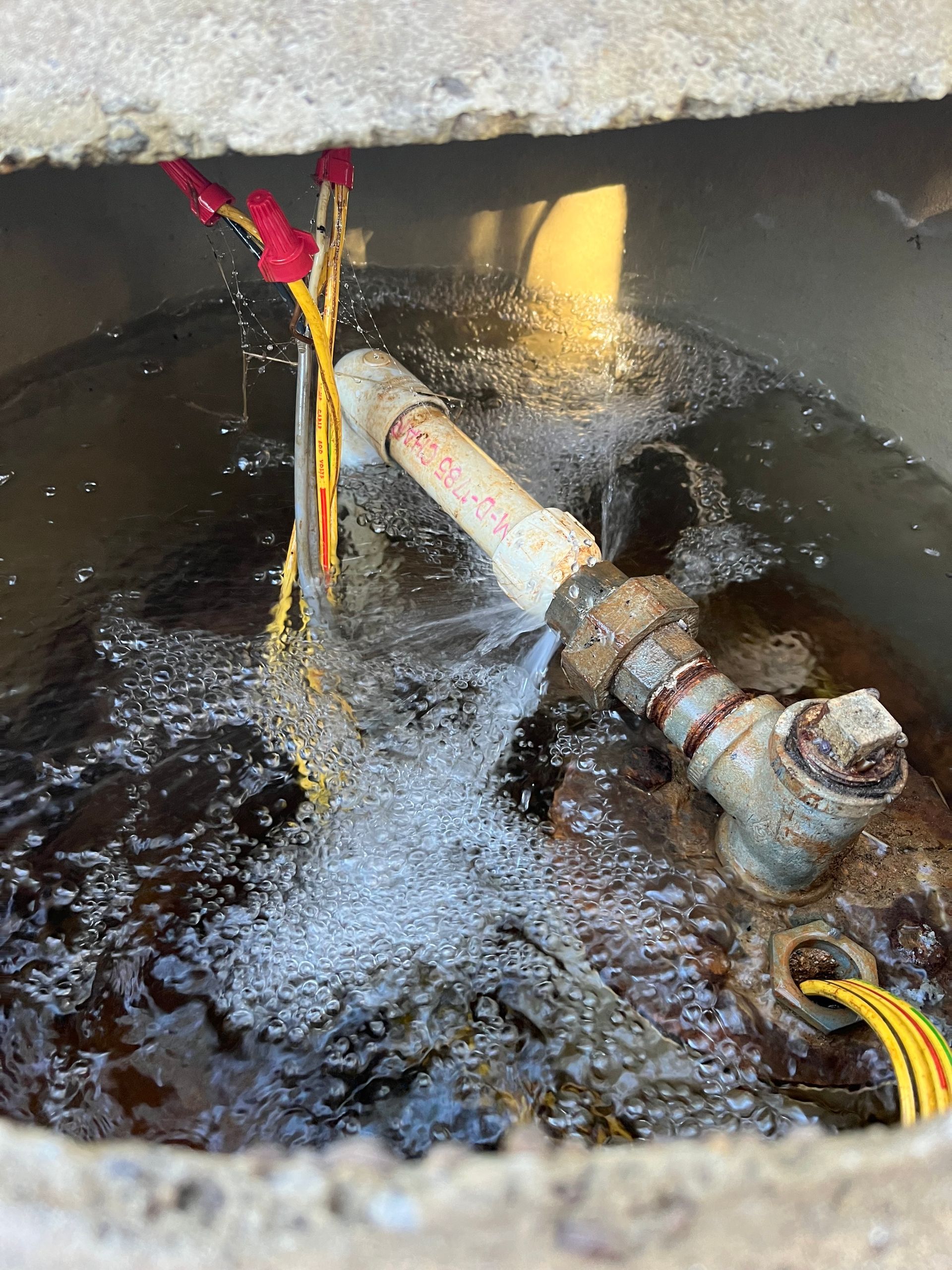 Broken underground pipe spraying water in a dark utility pit