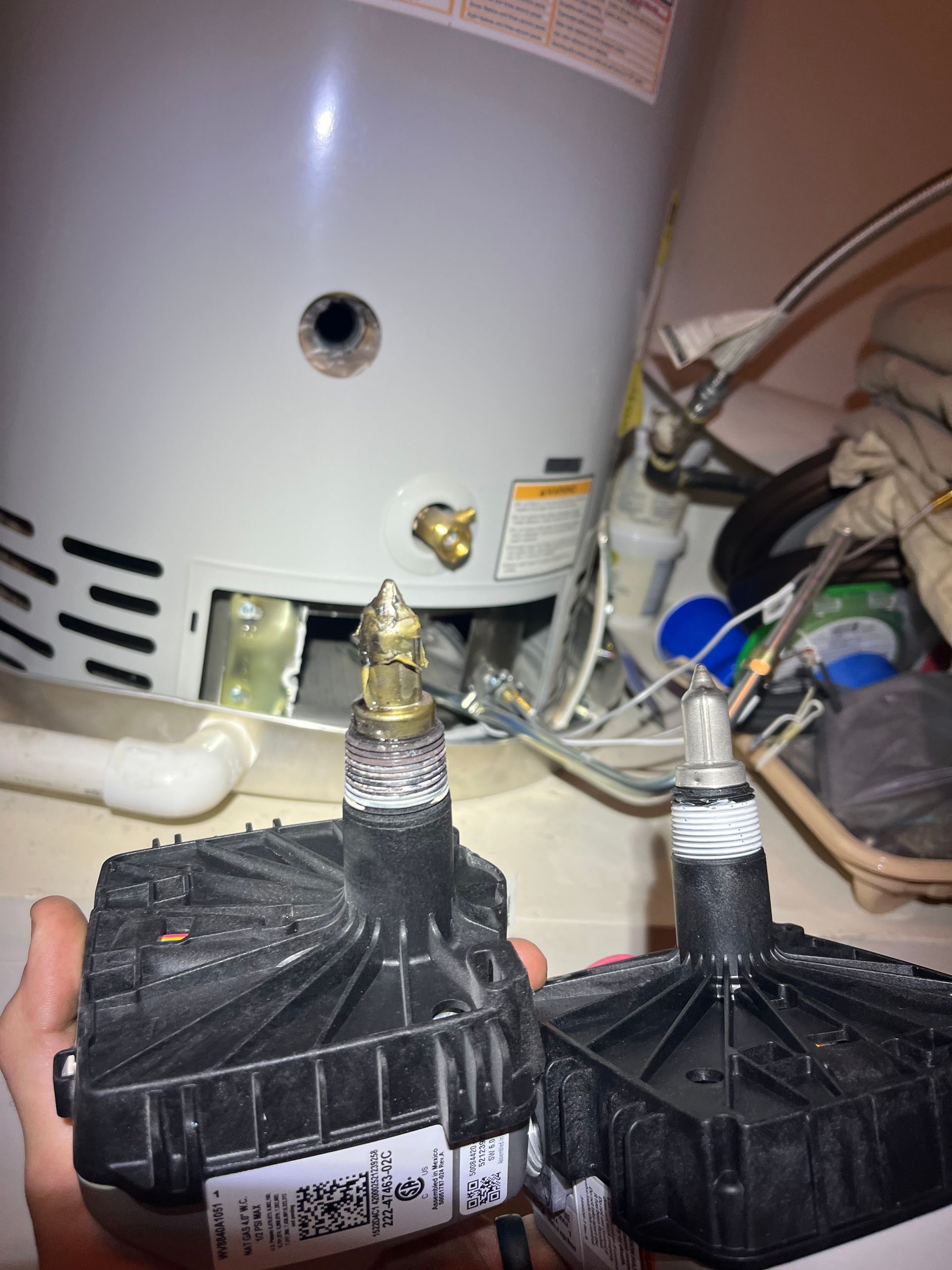 Water heater with two black insulated pipes and exposed fittings in a utility area.