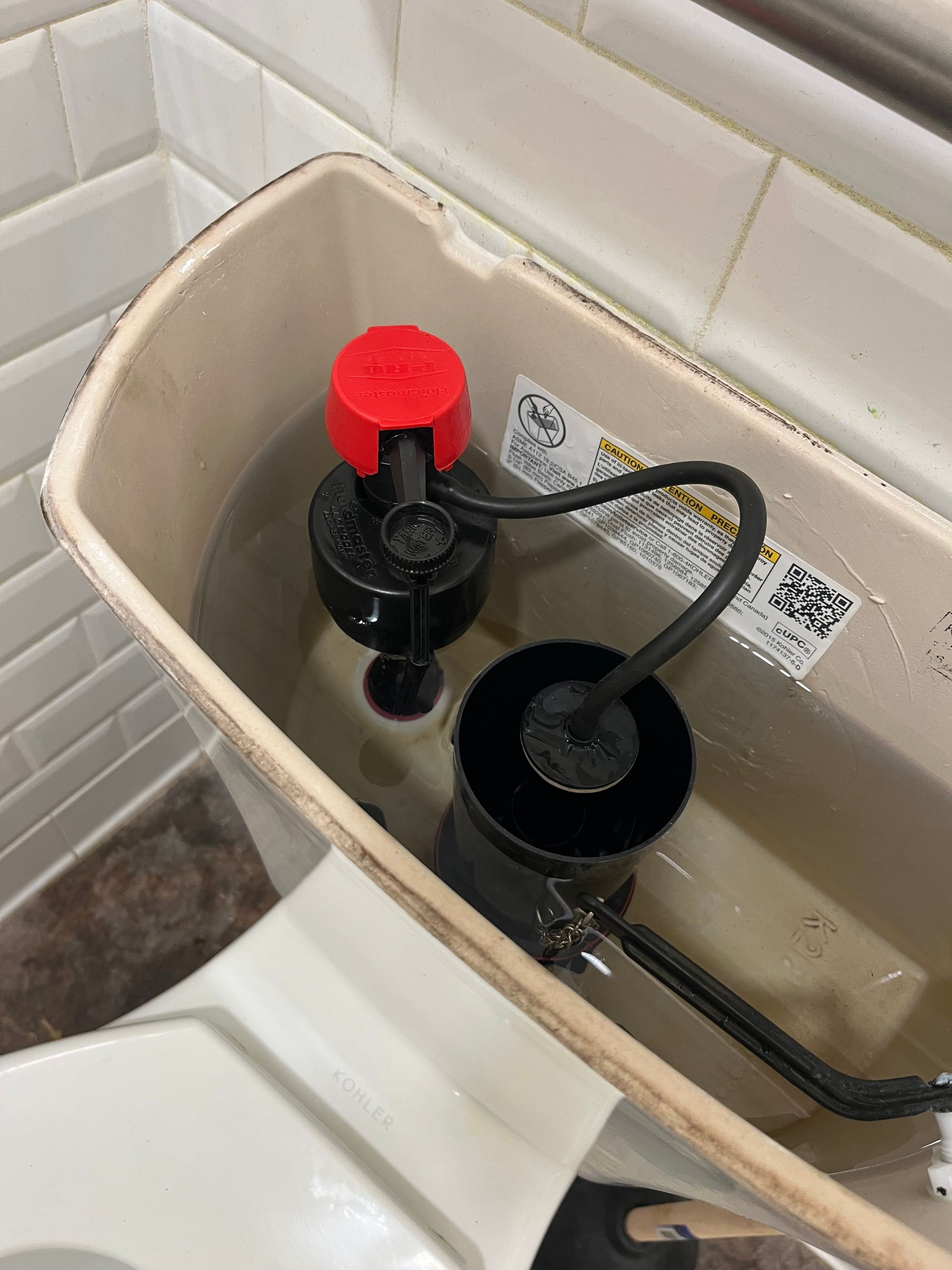 Toilet tank with a red flush valve and black fill valve inside a bathroom.