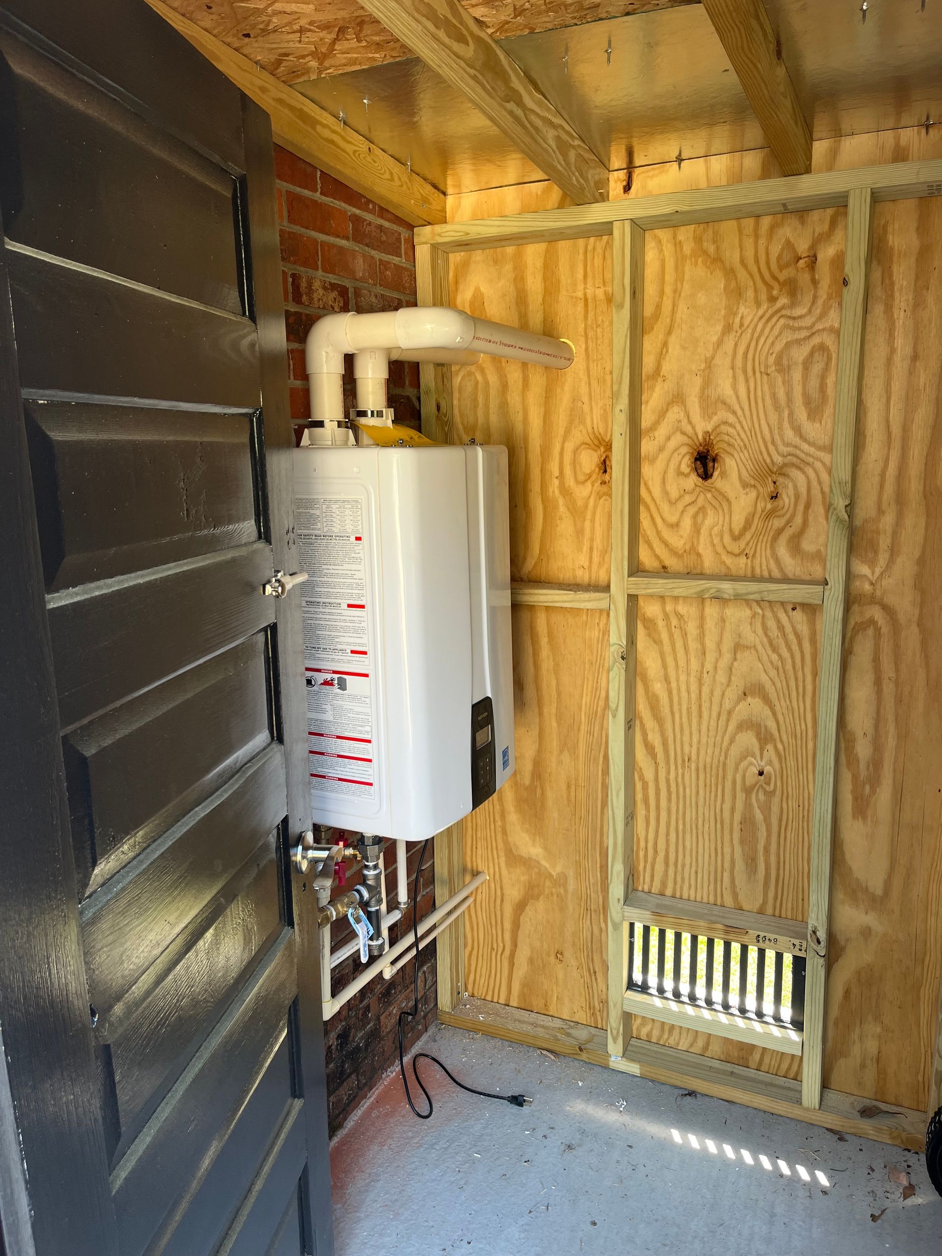 Utility room with a white water heater mounted beside exposed wooden wall framing.