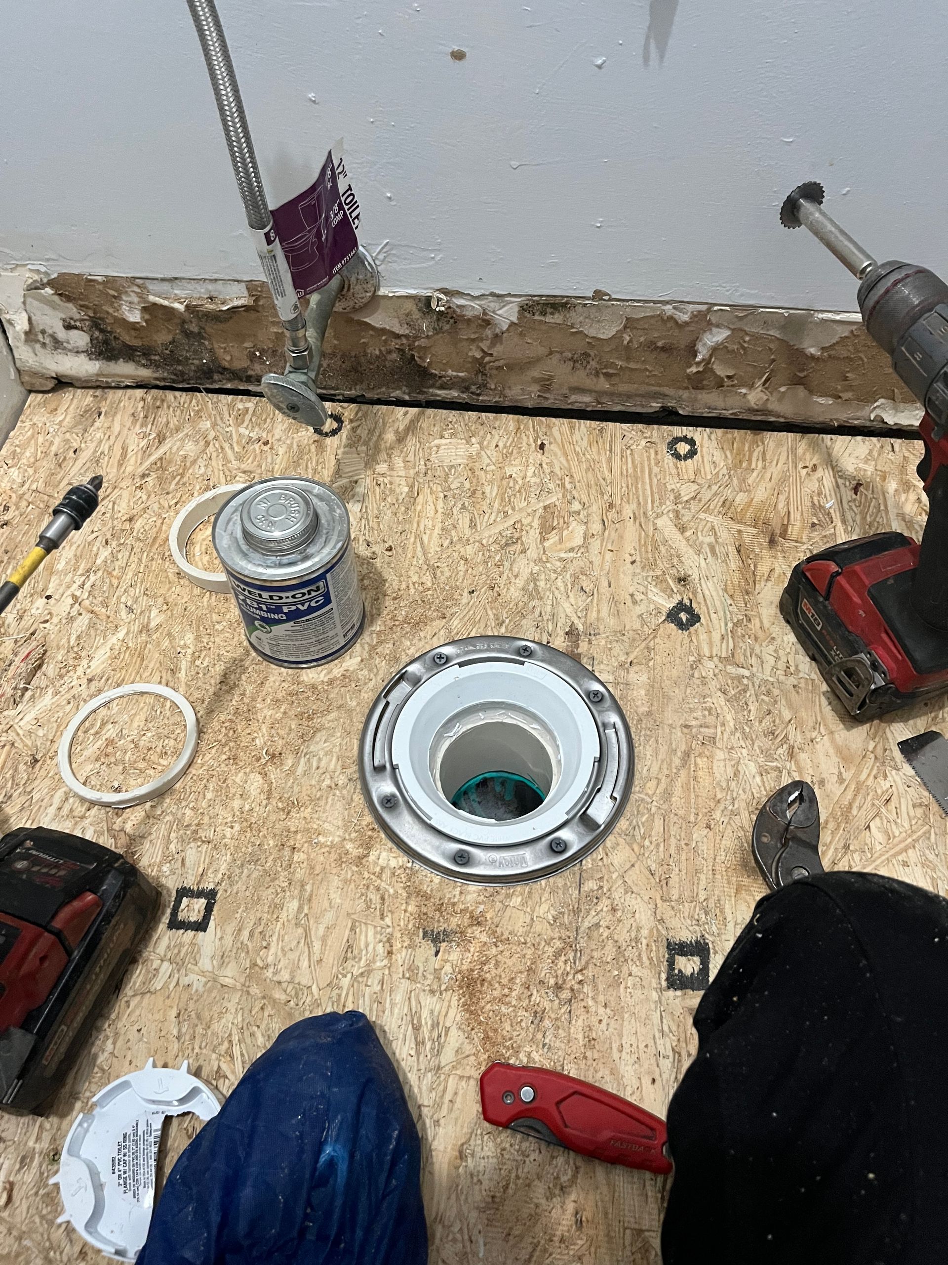 Bathroom floor under repair with tools, a pipe opening, and a circular drain fitting in the center.