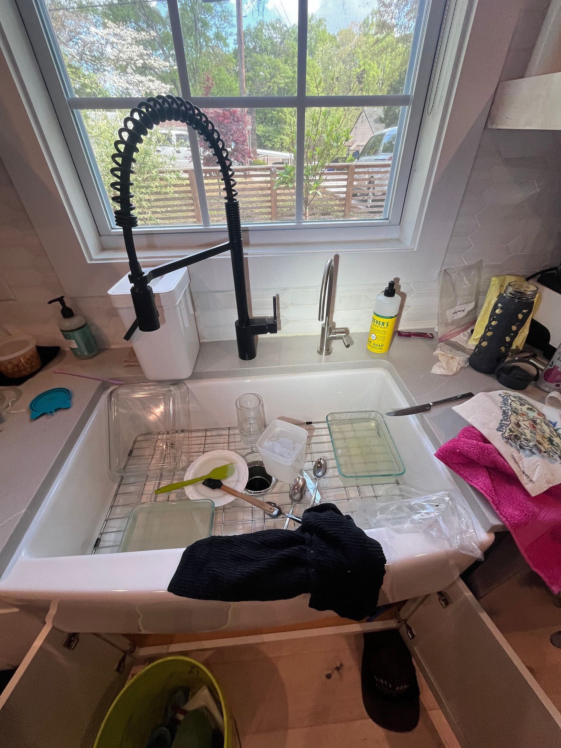 Cluttered kitchen sink under a window, with dishes, sponge, soap, and a black towel draped over the basin.