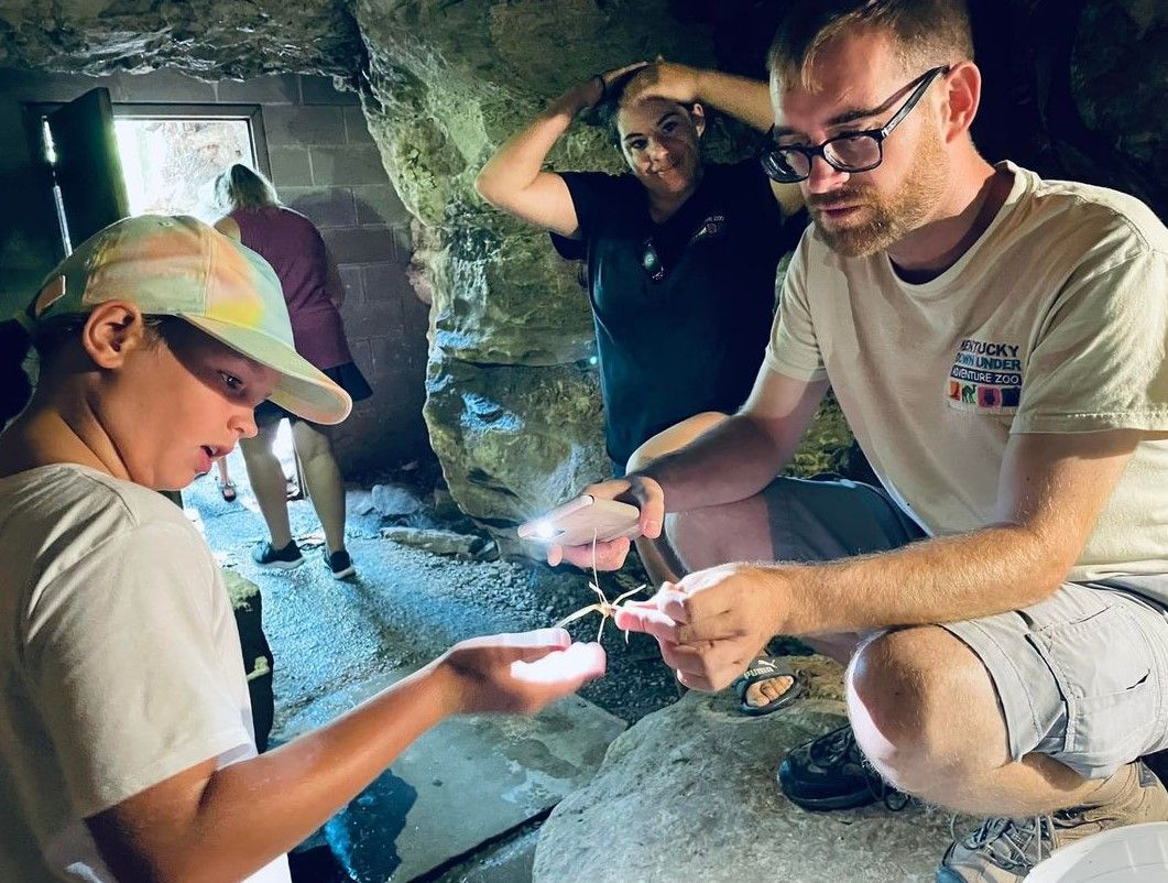 People exploring a rocky cave with flashlights, examining something glowing in their hands.
