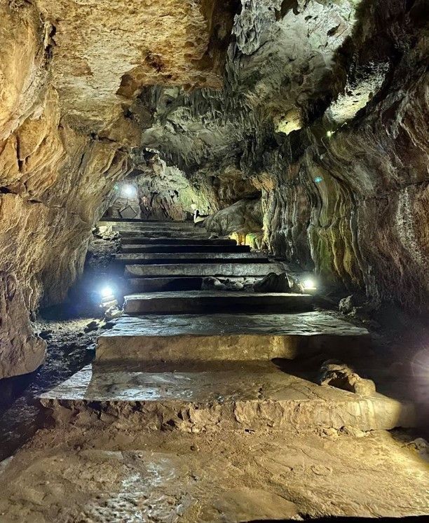 Lit cave staircase with stone steps, rough rock walls, and small lights illuminating the passage