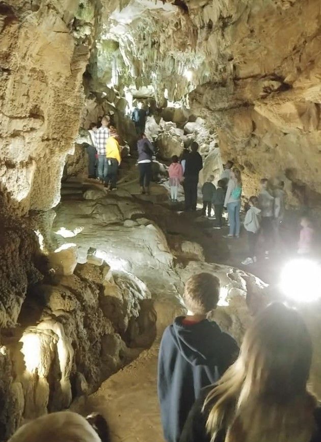 People walking through a rocky cave passage with bright lights and a wet floor