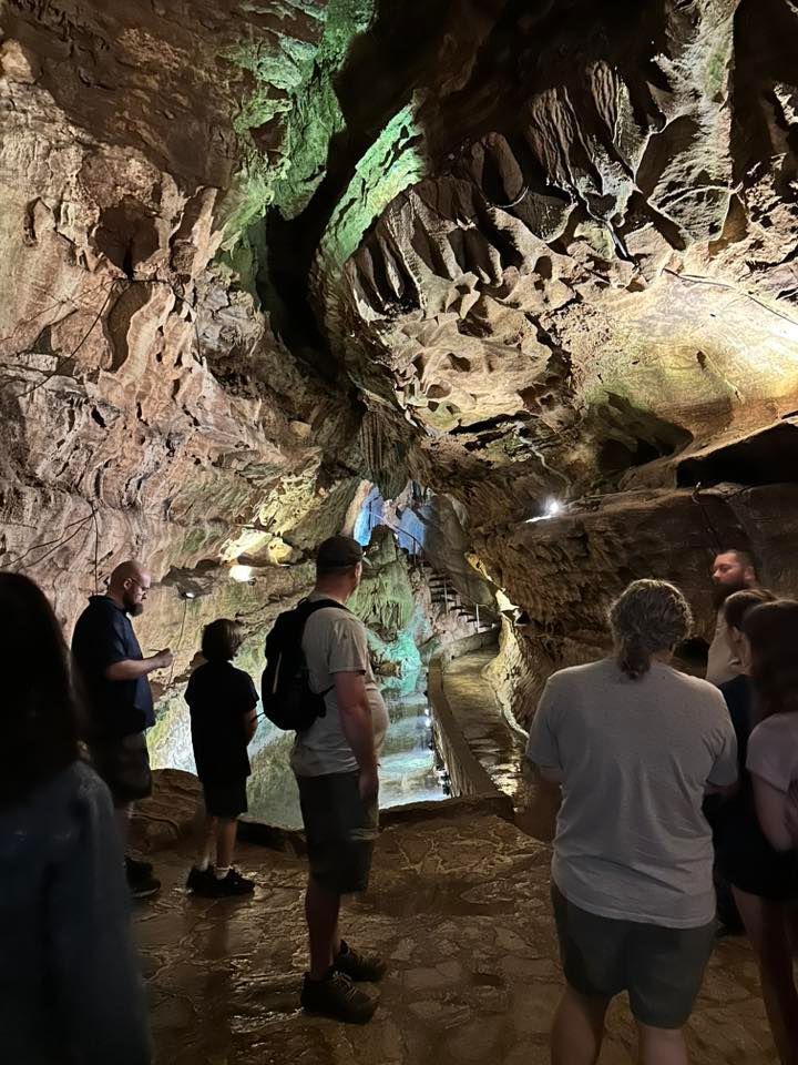 People standing in a rocky cave, looking up at illuminated rock formations.