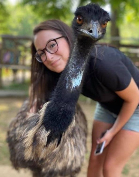 Woman posing with an emu outdoors, leaning close to its long neck.